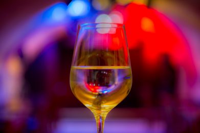 Auf dem Bild ist ein mit Weißwein gefülltes Weinglas vor buntem Scheinwerferlicht zu sehen.