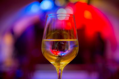 Auf dem Bild ist ein mit Weißwein gefülltes Weinglas vor buntem Scheinwerferlicht zu sehen.