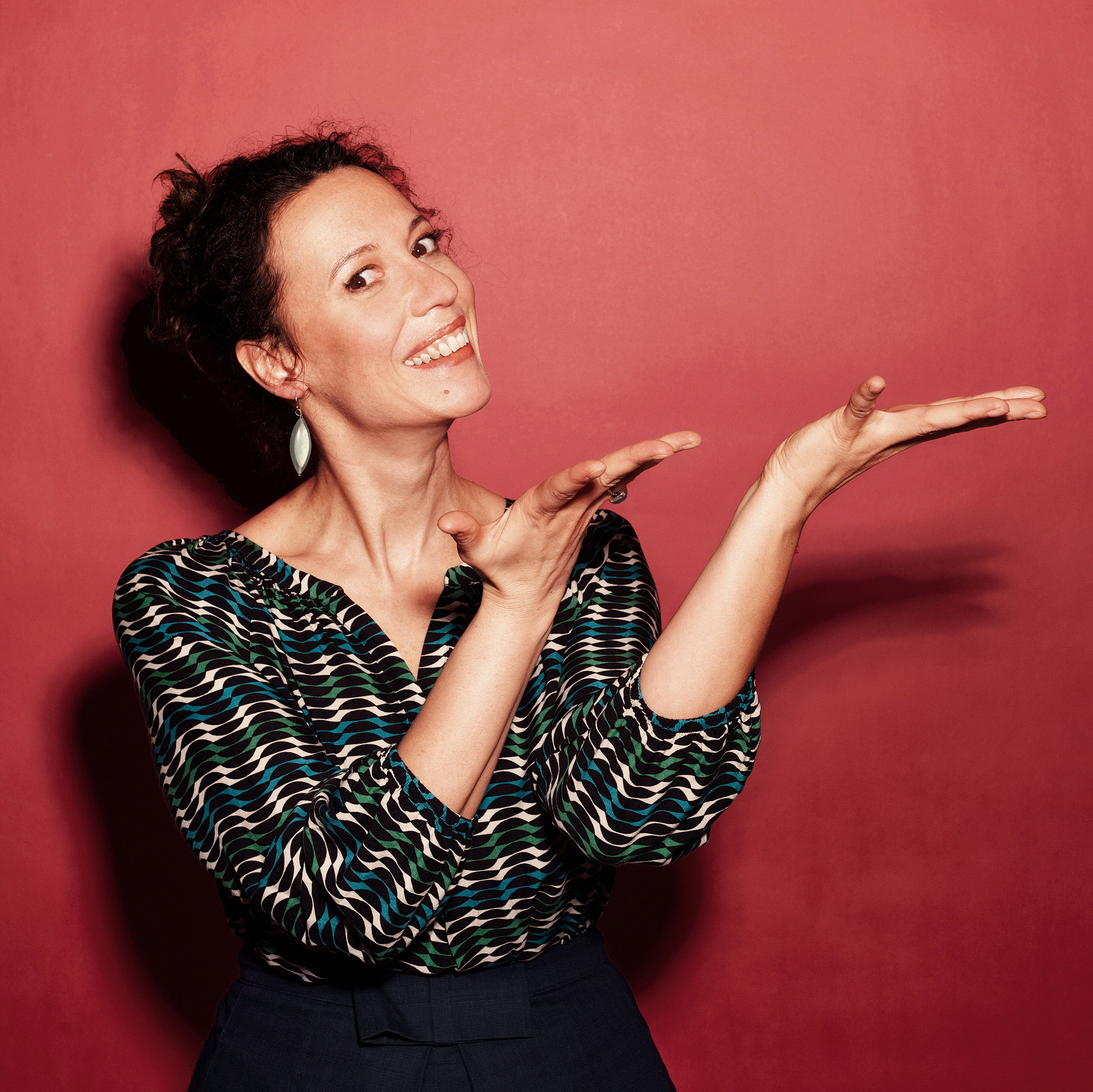 Auf dem Foto ist die Musikkabarettistin Alice Köfer vor rotem Hintergrund zu sehen.
