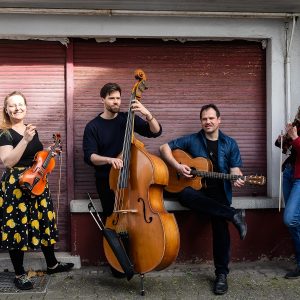 Auf dem Bild ist das Quartett Feinschmeckerfolk mit seinen Instrumenten vor einem alten heruntergelassenen Rolladen zu sehen.