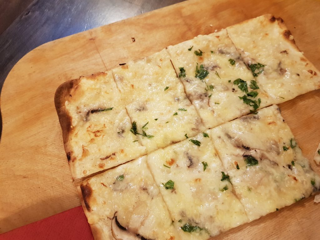 Auf dem Bild ist ein Flammkuchen auf dem Holzbrett zu sehen.
