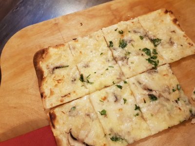 Auf dem Bild ist ein Flammkuchen auf dem Holzbrett zu sehen.