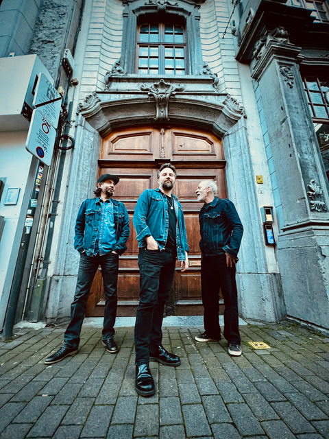 Auf dem Bild sind die drei Musiker vom Gerry Hundt Trio vor einem mächtigen Holzportal stehend zu sehen.