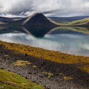 Auf dem Bild ist eine isländische Landschaft mit Hügeln und See zu sehen.