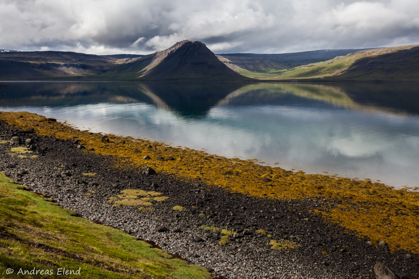 Auf dem Bild ist eine isländische Landschaft mit Hügeln und See zu sehen.