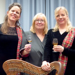 Auf dem Foto sind die Autorin und die beiden Musikerinnen jeweils mit einem Glas in der Hand zu sehen.