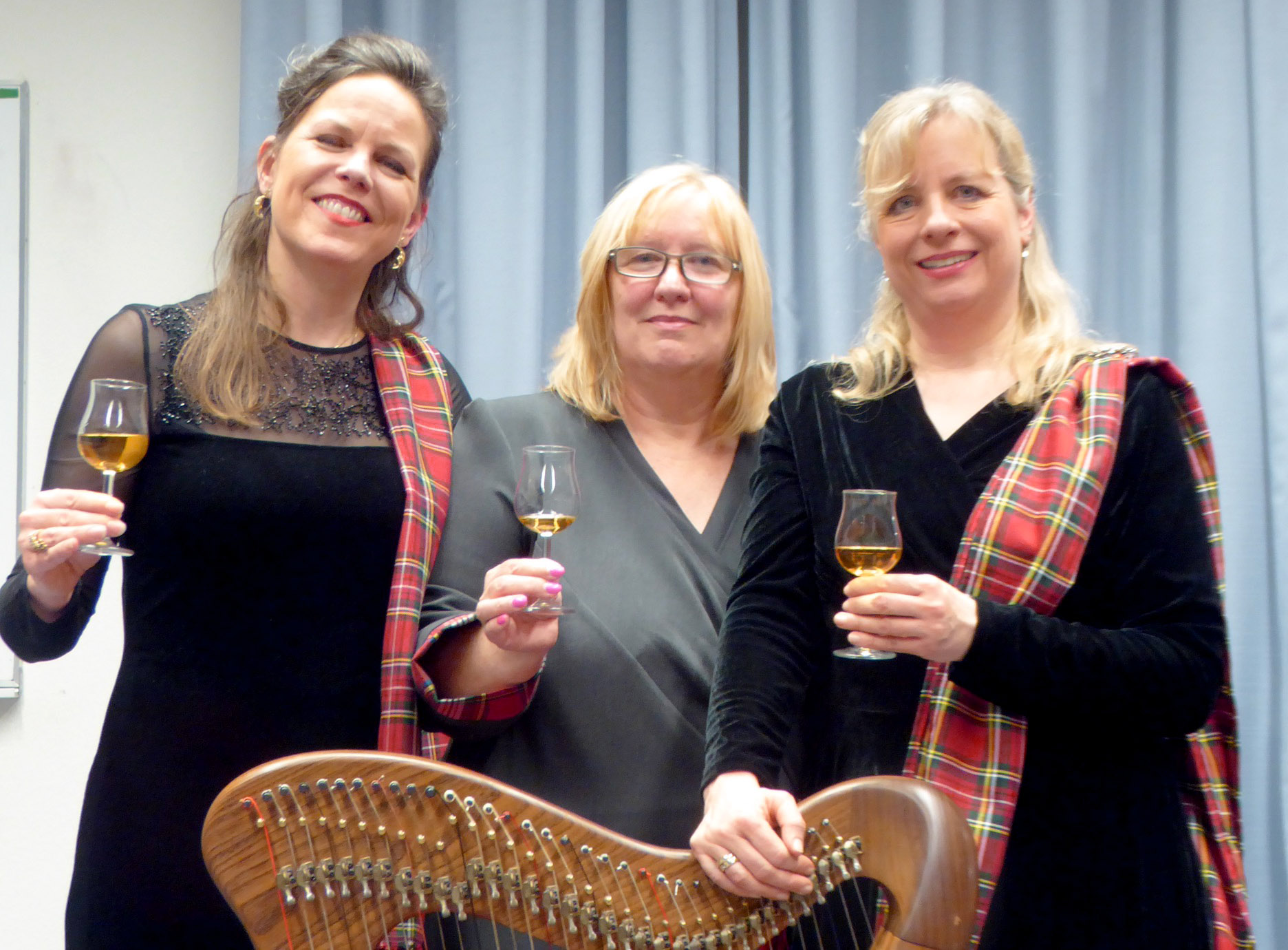 Auf dem Foto sind die Autorin und die beiden Musikerinnen jeweils mit einem Glas in der Hand zu sehen.