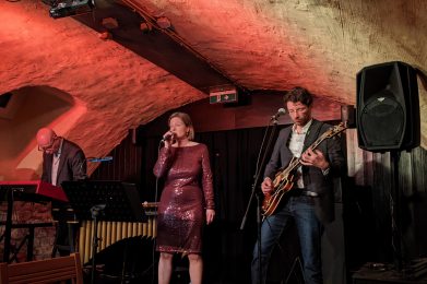 Auf dem Bild sind die drei Musiker von Trois à la fois auf der Bühne in Garniers Keller zu sehen.