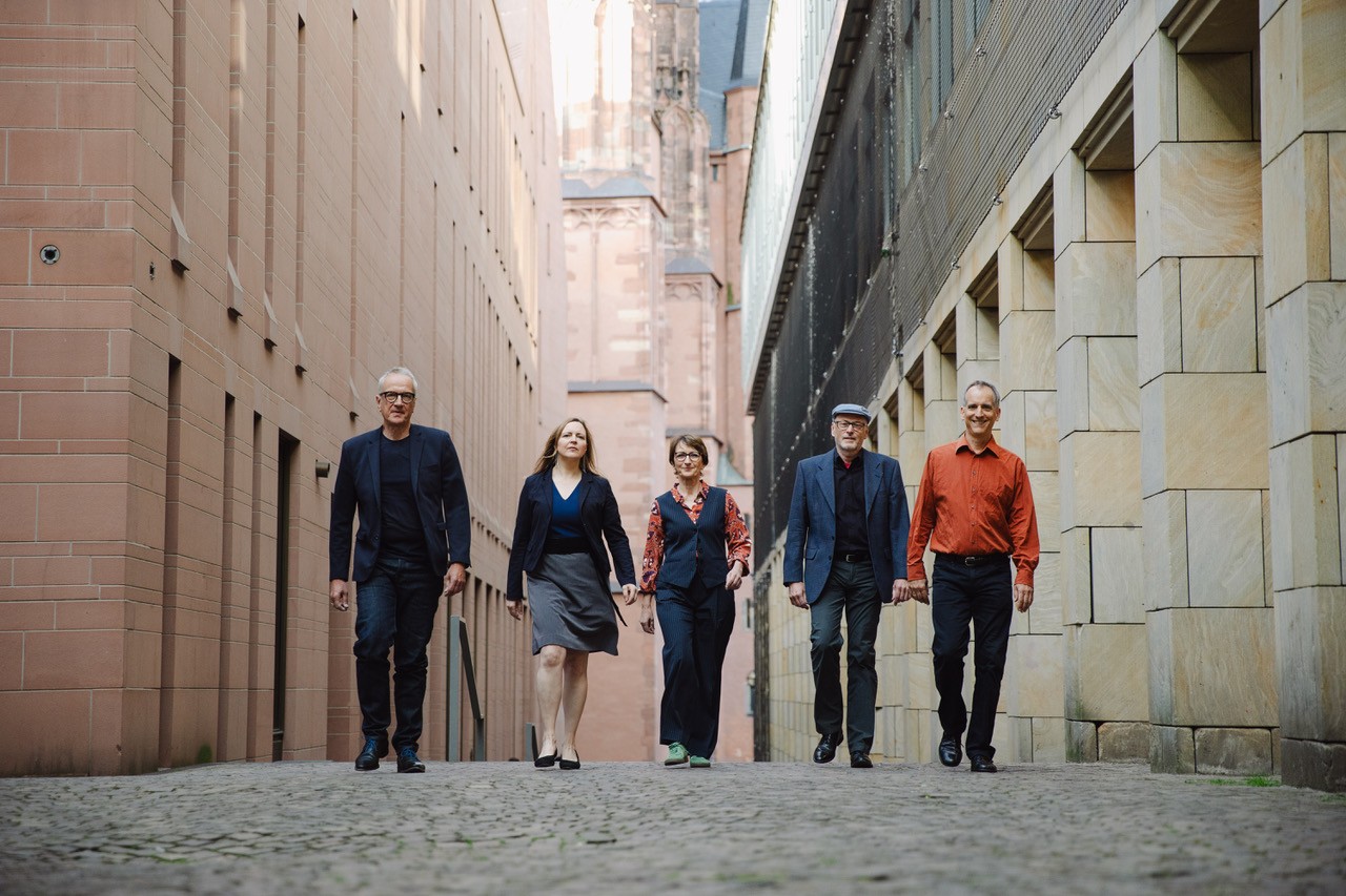 Auf dem Foto sind die fünf Musiker von Pia and the Ambassadors zu sehen, die durch eine Häuserschlucht gehen.