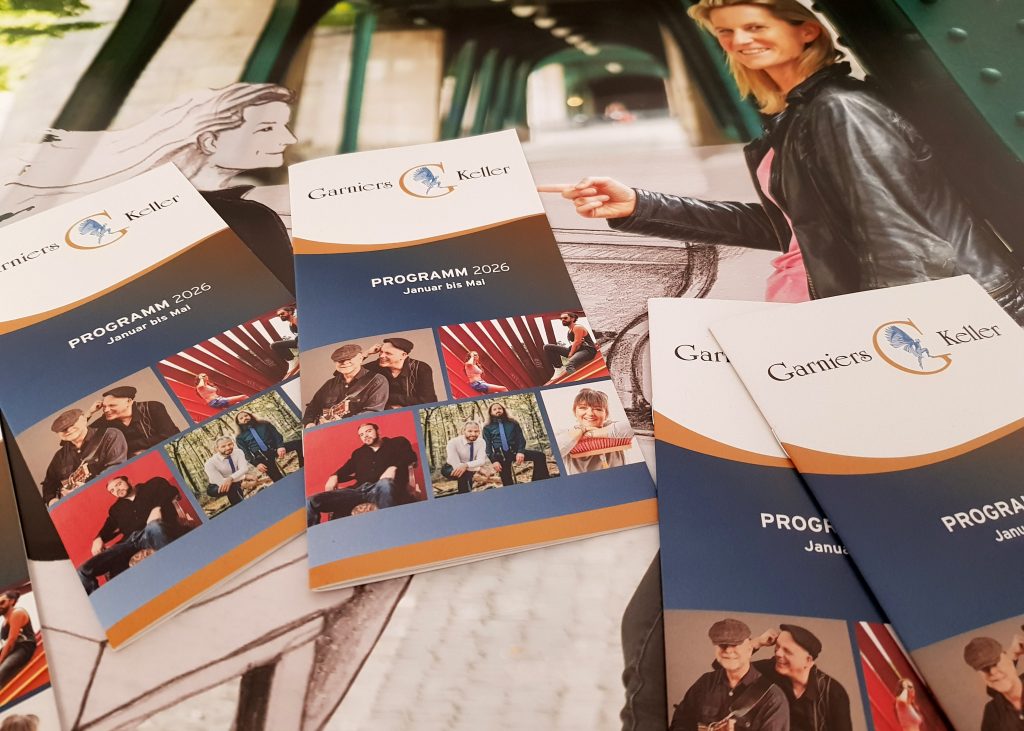 Auf dem Bild sind aktuelle Programmhefte vom Garnies Keller auf einem Plakat liegend zu sehen.