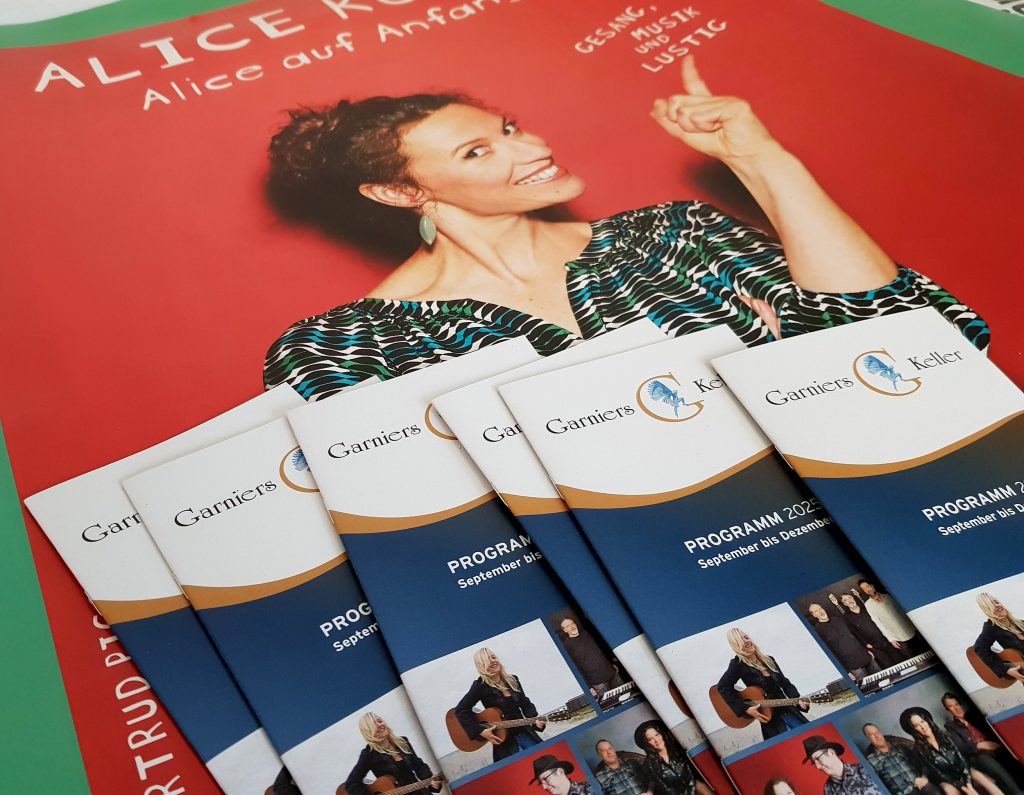 Auf dem Bild sind mehrere Programmhefte vom Garniers Keller auf einem Plakat von Alice Köfer liegend zu sehen.