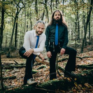 Auf dem Bild sind die beiden Musiker von Stout im Wald stehend zu sehen.