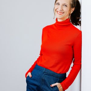 Auf dem Bild ist Sarah Hakenberg in einem roten Rollkragenpullover zu sehen.