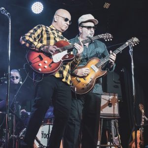 Auf dem Fotos sind zwei Musiker der Band The Too Bad Jims mit Instrumenten auf der Bühne zu sehen.